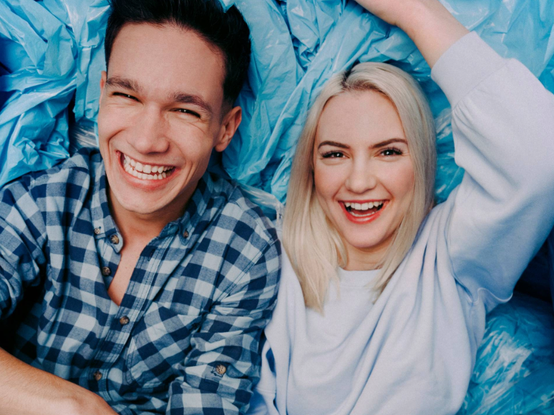 Veselý muž v károvanej košeli a usmievajúca sa žena v bielom svetri sú obklopení modrými plastovými taškami.